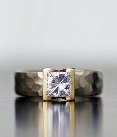 a gold and silver ring with a square cut diamond in the center on a reflective surface