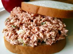 a tuna salad sandwich on a bagel bun with an apple in the background