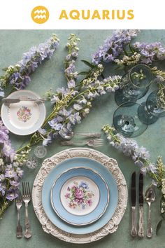 the table is set with plates, silverware and purple flowers on top of it