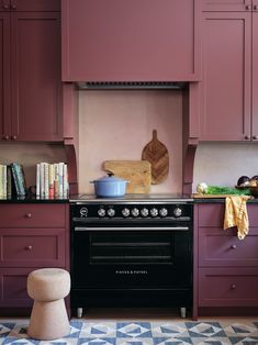 a stove top oven sitting inside of a kitchen next to purple cupboards and drawers