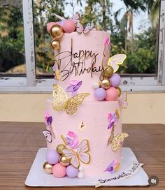 a pink birthday cake with gold butterflies on it and the words happy birthday written on top