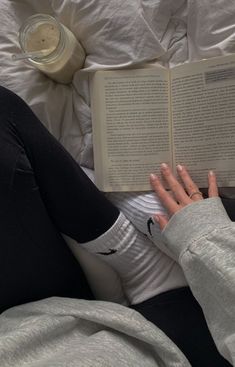 a woman laying in bed reading a book with her hand on top of the book