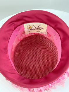 "What a beauty! Tall 1960s pink flowered hat covered by pink netting. Satin brim. Made by Parke Layne. Size 21\". Stands 6\" tall. Very good condition." Retro Pink Wide Brim Hat, Retro Pink Brimmed Hat, Vintage Pink Adjustable Mini Hats, Pink Retro Party Hats, Pink Vintage Costume Hat For Parties, Pink Vintage Wide Brim Hat, Pink Bucket Hat For Kentucky Derby, Vintage Pink Party Hat And Headpiece, Vintage Pink Mini Hat For Party