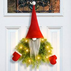 a christmas wreath with a gnome's head hanging from the front door and lights on it