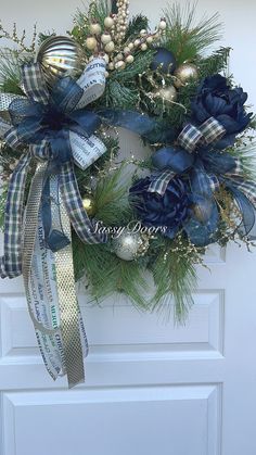 a christmas wreath hanging on the front door with blue and white ribbons, pine cones, berries and bells