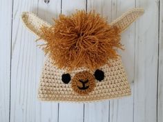 a crocheted llama hat hanging from a hook on a white wooden wall