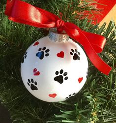 a white ornament with black and red paw prints on it hanging from a christmas tree