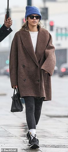 a woman walking down the street with an umbrella in her hand and another person holding an umbrella behind her