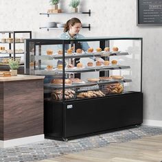 a woman standing behind a counter filled with donuts and pastries in a bakery