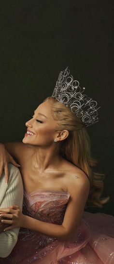 a woman wearing a tiara sitting next to a man in a ball gown and holding his arm around her chest