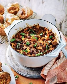 a white pot filled with food on top of a wooden table next to other foods