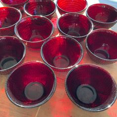 a bunch of red glass bowls sitting on top of a wooden table next to each other