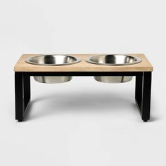 two stainless steel bowls sit on a wooden table with black legs and base for the elevated dog bowl