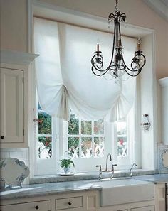 a chandelier hangs from the ceiling in a kitchen with white cabinets and marble counter tops