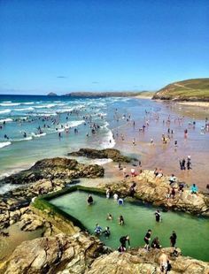 many people are swimming in the water near rocks and sand at the beach on a sunny day