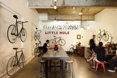 people sitting at tables with bicycles hanging from the ceiling in a room filled with bikes