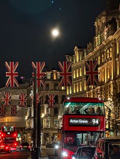 a red double decker bus driving down a street next to tall buildings with flags on them