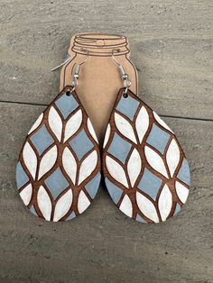 two pairs of blue and white leather earrings on the ground next to a mason jar