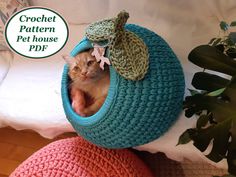 a cat is sitting in a crocheted ball on top of two pillows and a plant