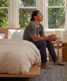 a man sitting on top of a bed next to a table with a cup in it