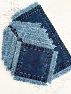 four pieces of denim with frayed edges on a white surface, one is folded and the other has been cut in half