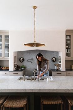 a woman is standing at the sink in a kitchen with marble counter tops and stools