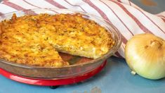 a pie sitting on top of a red pan next to an onion