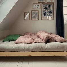 an unmade bed with pillows and blankets on it in a room under a slanted ceiling