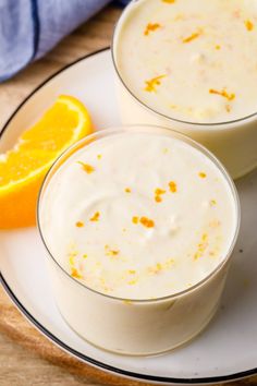 two glasses filled with white liquid sitting on top of a plate next to an orange slice