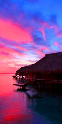 the sun is setting over an ocean with boats in it and thatched huts on stilts