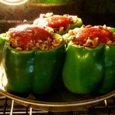 three green peppers stuffed with rice and sauce on an oven rack, ready to be cooked