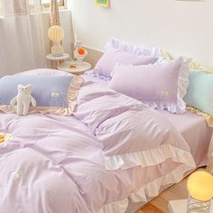 there is a bed with purple sheets and pillows on the floor next to a window