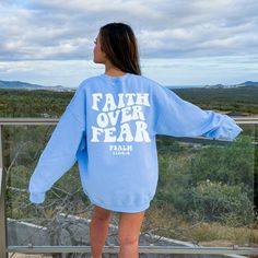 a woman in a blue sweatshirt standing on a balcony looking out at the hills and trees