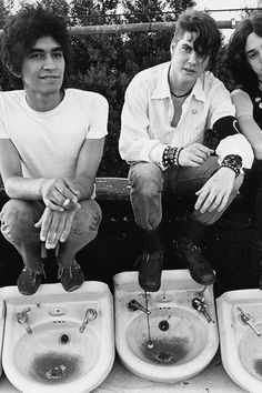 four young men sitting on top of urinals next to each other