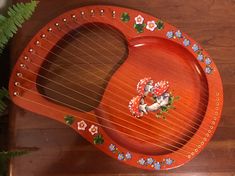 a wooden instrument with flowers painted on the top and sides, sitting next to a potted plant