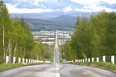 an empty road with trees and mountains in the backgrouds, surrounded by greenery