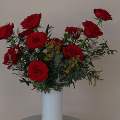 a white vase filled with red roses on top of a table