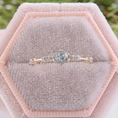 an engagement ring with blue topaz sits on a pink velvet box