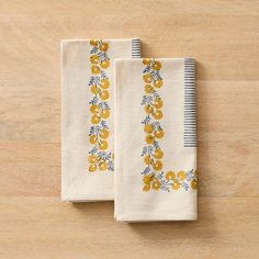 two white towels with yellow flowers on them sitting on top of a wooden table next to each other