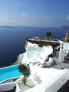 an outdoor swimming pool on the side of a cliff overlooking the water and mountains in the distance