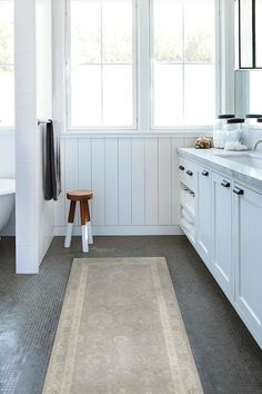 a bathroom with white walls and gray rugs on the floor, along with two windows