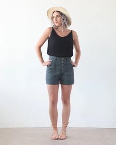 a woman standing in front of a white wall with her hands on her hips wearing a hat