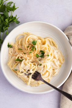 a white bowl filled with pasta and parsley on top of a table next to a napkin