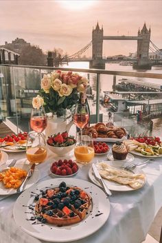 a table filled with food and drinks on top of a white table cloth next to a river