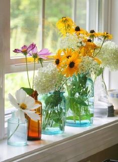 three vases filled with different types of flowers on a window sill next to a window