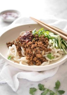 a white bowl filled with noodles and meat next to chopsticks on a table