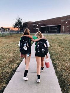 two girls walking down a sidewalk carrying backpacks