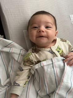 a baby laying on top of a bed covered in a blanket and looking at the camera