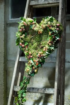 a heart shaped wreath on top of an old wooden ladder with moss growing out of it