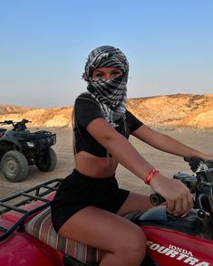 a woman riding on the back of a red four - wheeler with a bandanna over her head